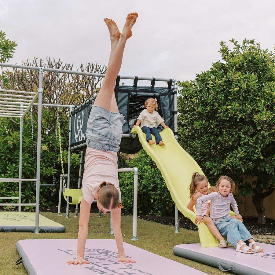 Child doing handstand beside yellow Cubby Clubhouse slide
